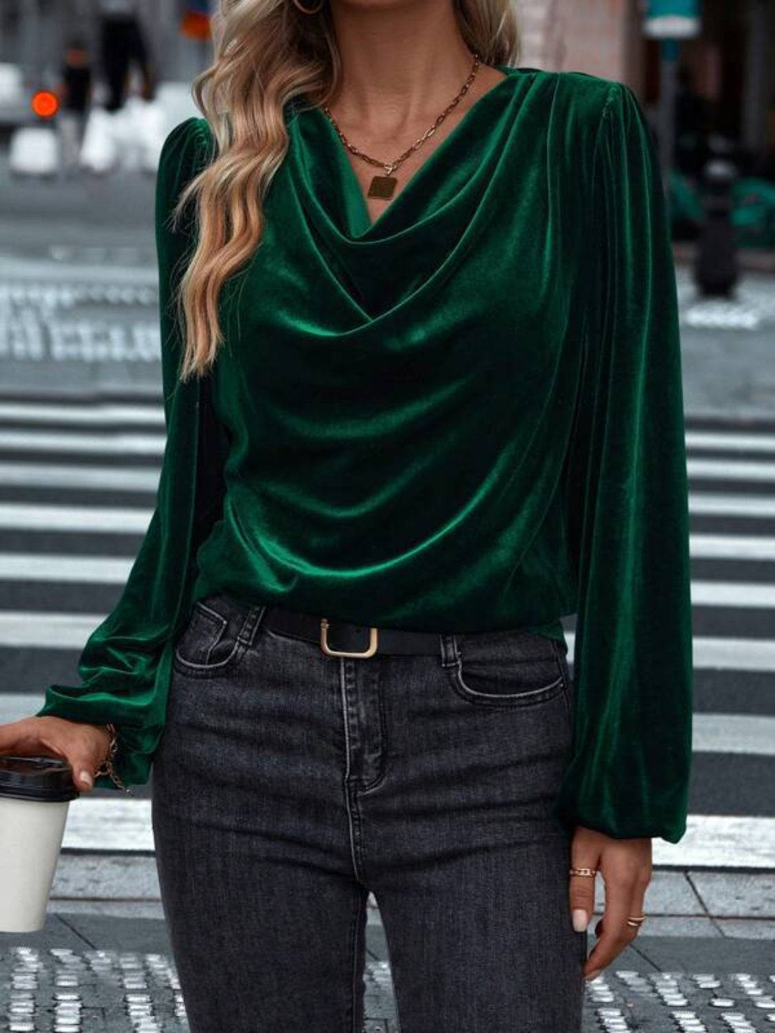 Model wearing a dark green Lovelet cowl neck long sleeve blouse, styled with jeans against a festive backdrop.