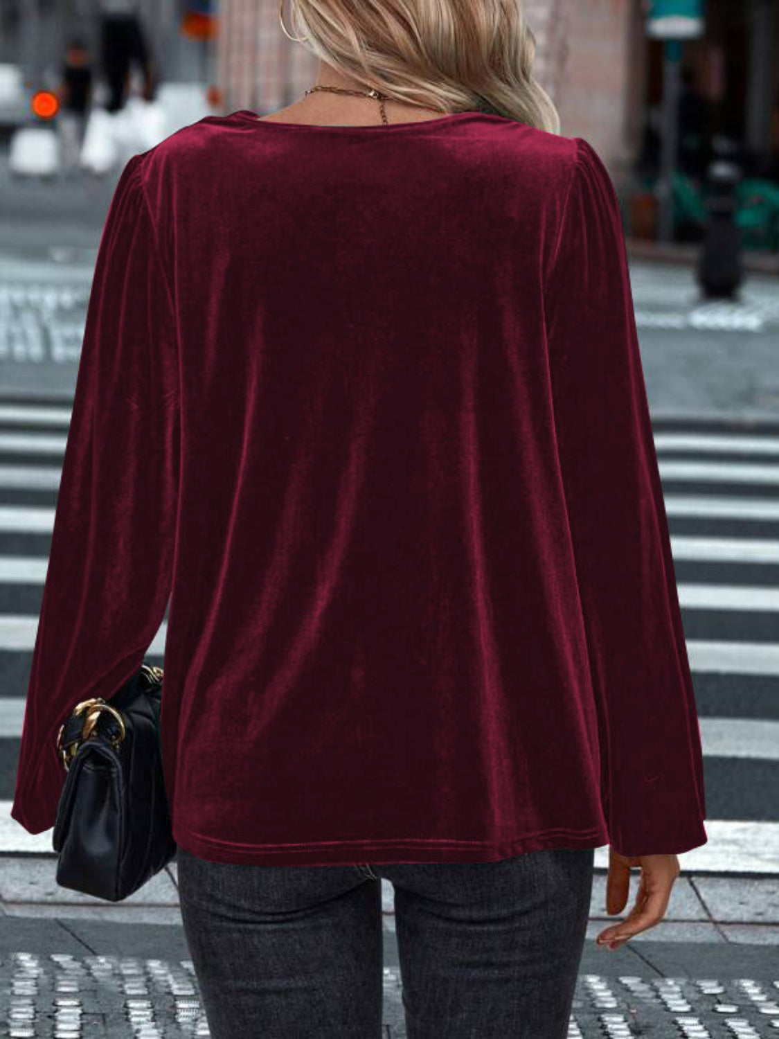 Woman wearing a burgundy Lovelet cowl neck long sleeve blouse, seen from the back on a city street.