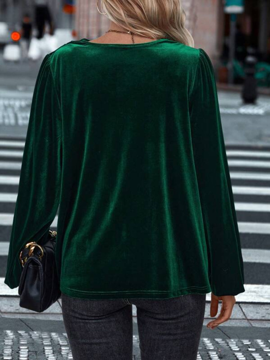 Model wearing a dark green Lovelet cowl neck long sleeve blouse, styled with jeans against a festive backdrop.