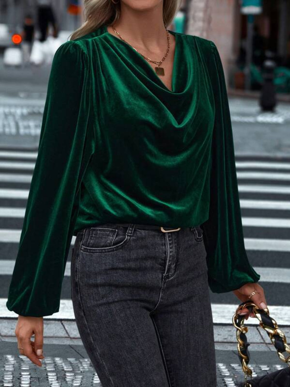 Model wearing a dark green Lovelet cowl neck long sleeve blouse, styled with jeans against a festive backdrop.