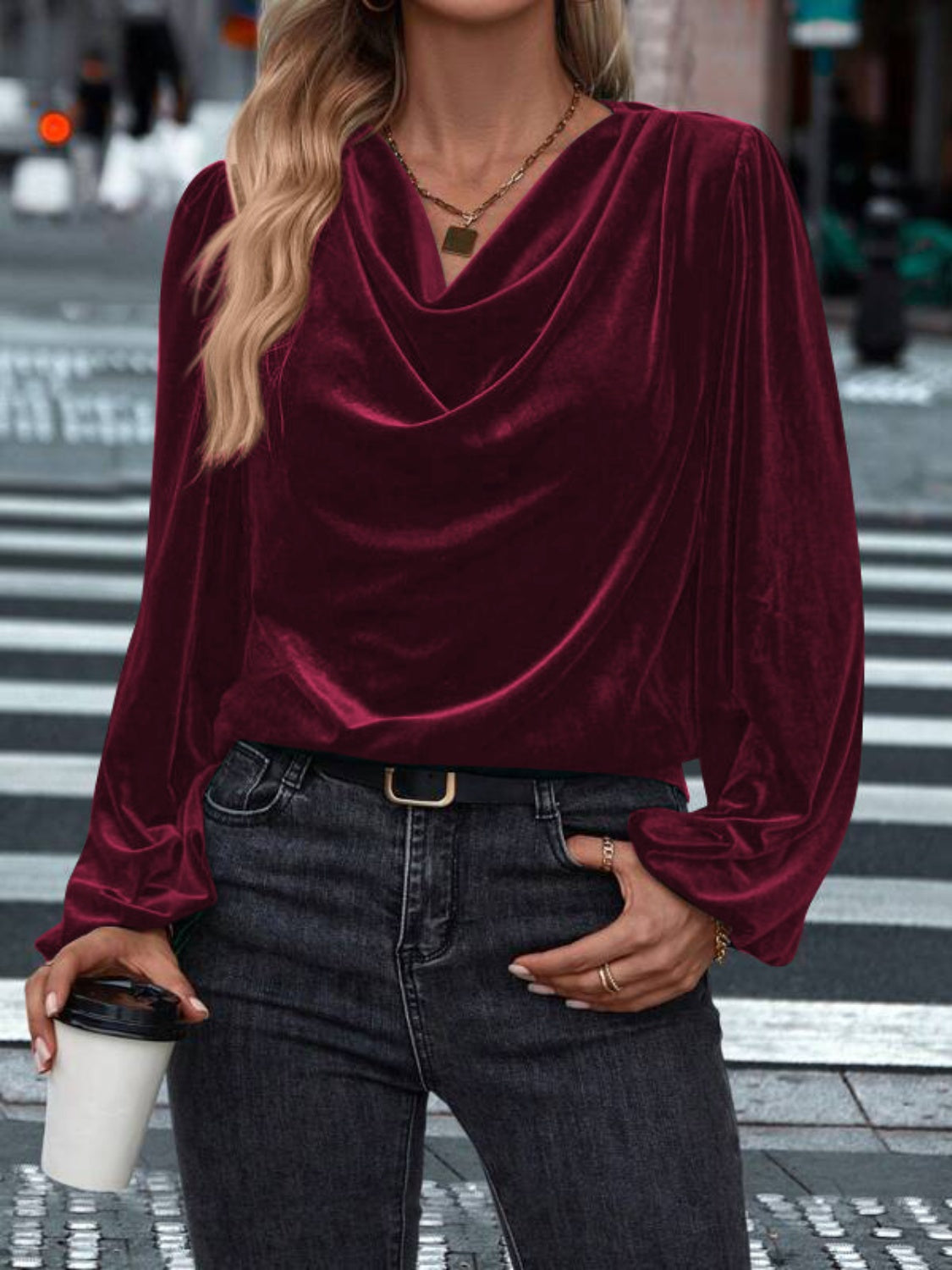 Model wearing a burgundy Lovelet cowl neck long sleeve blouse, styled with jeans against a festive backdrop.