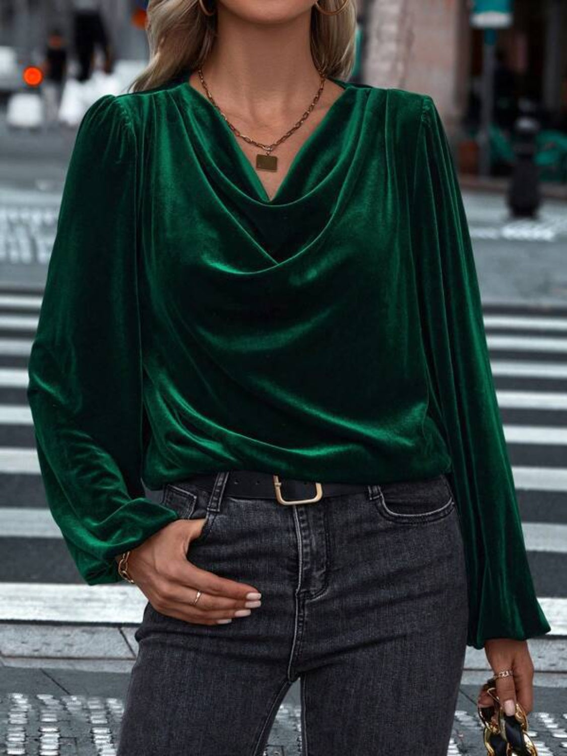 Model wearing a dark green Lovelet cowl neck long sleeve blouse, styled with jeans against a festive backdrop.